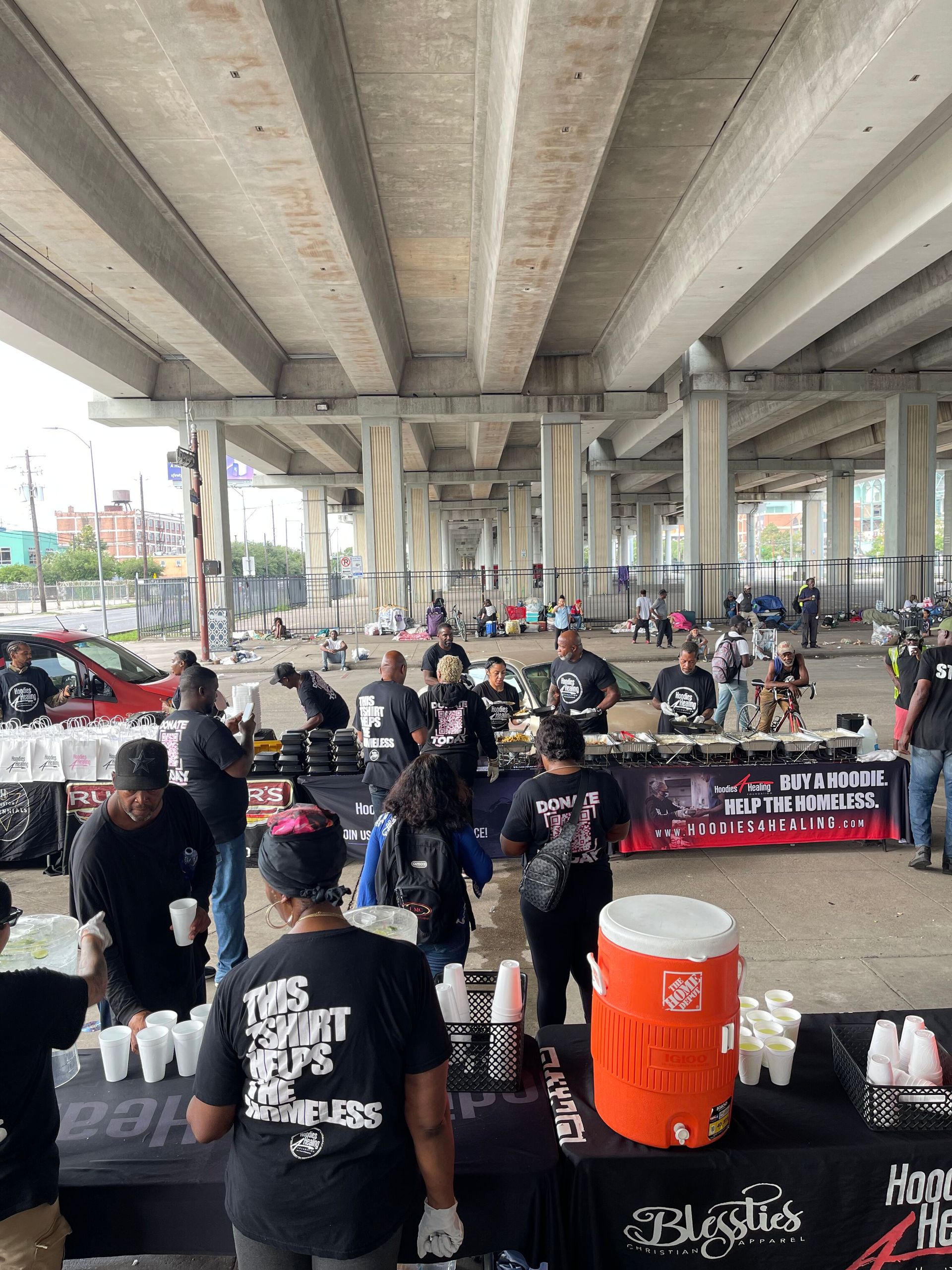A group of people are standing around tables under a bridge.
