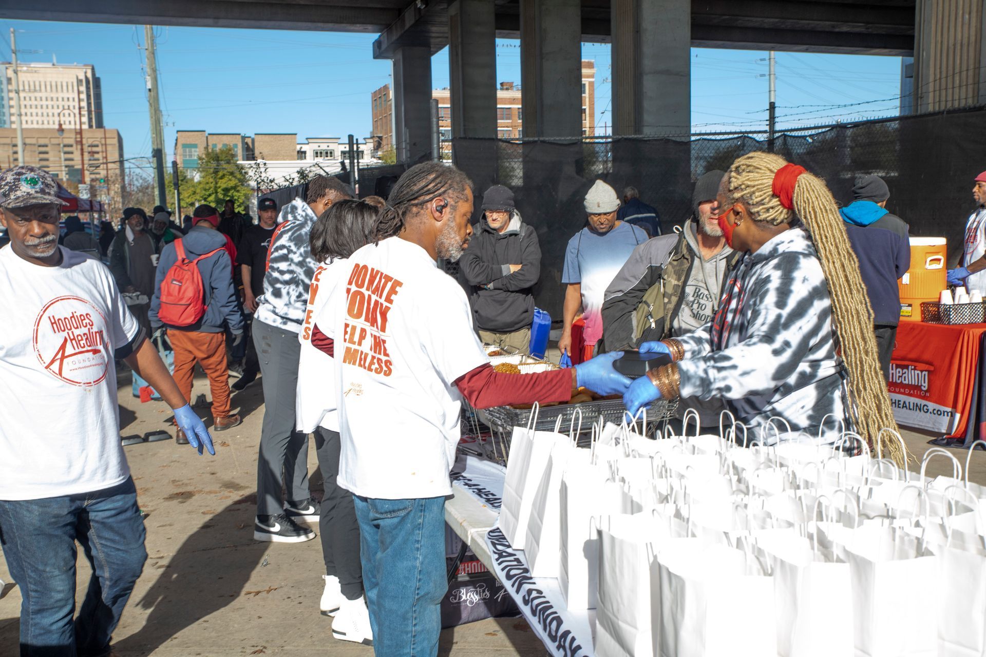 A group of people are standing around a table with bags of food.