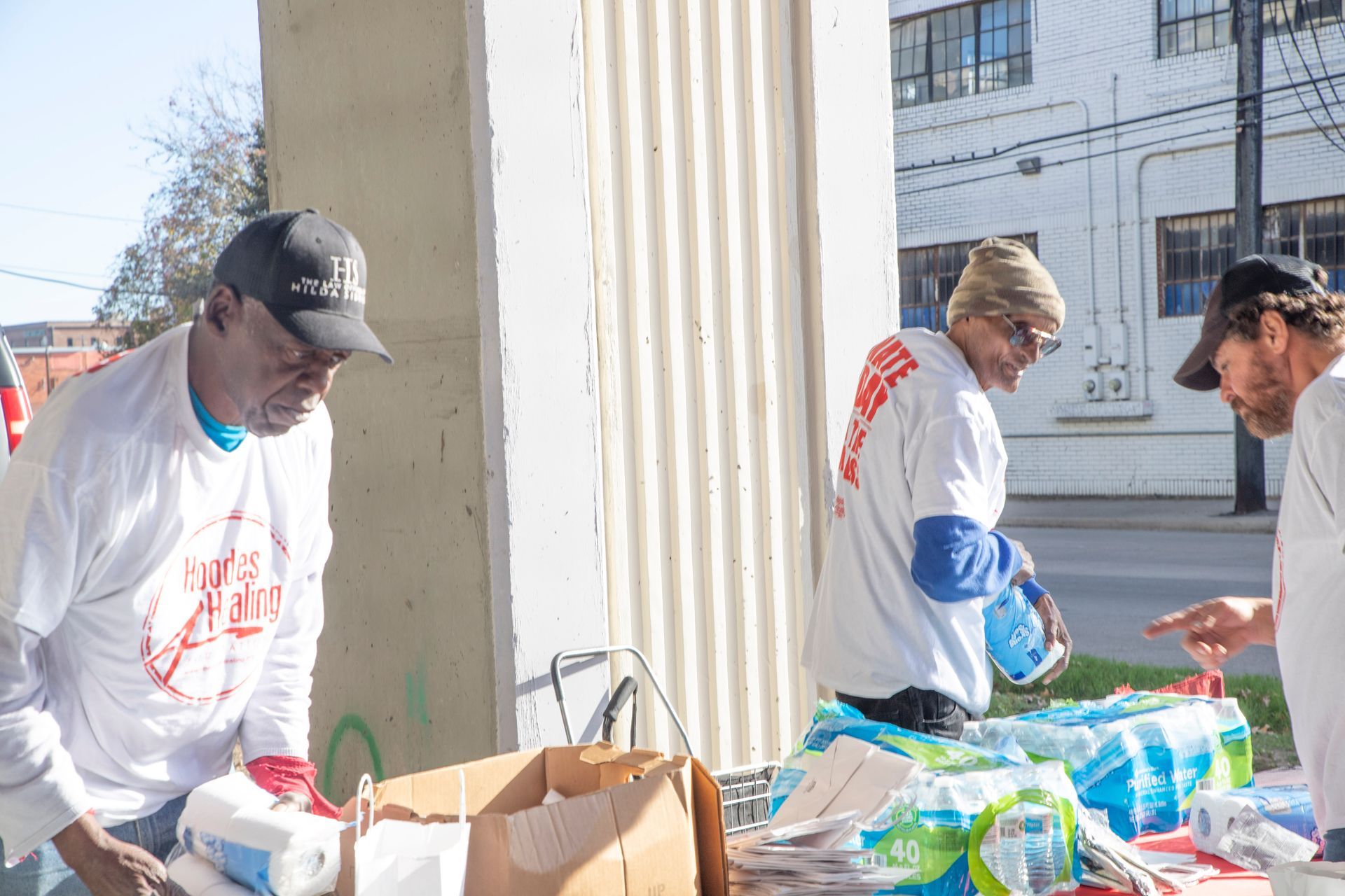 Three men are standing around a table filled with bottles of water.