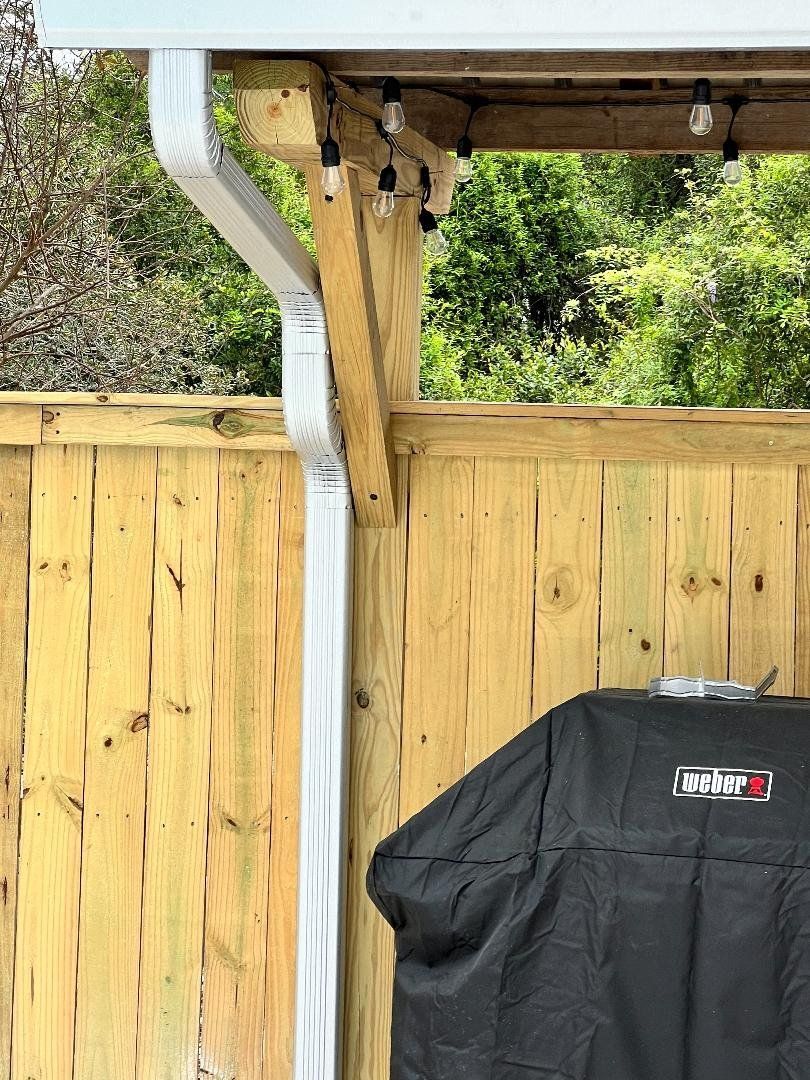 A grill is sitting under a roof next to a wooden fence.