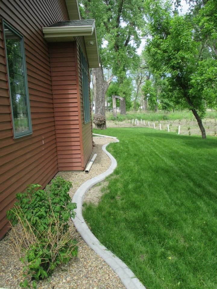 Brown house with green lawn, a wavy concrete edging, and a green tree in the background.