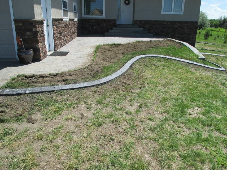 Front yard with concrete walkway, partial grass, and stone facade on a beige house.