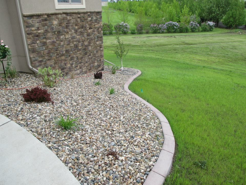 A landscaped front yard with a stone bed, edging, and green lawn.
