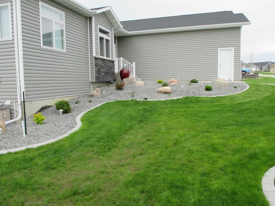 A gray-sided house with a curved rock garden bordering bright green grass.