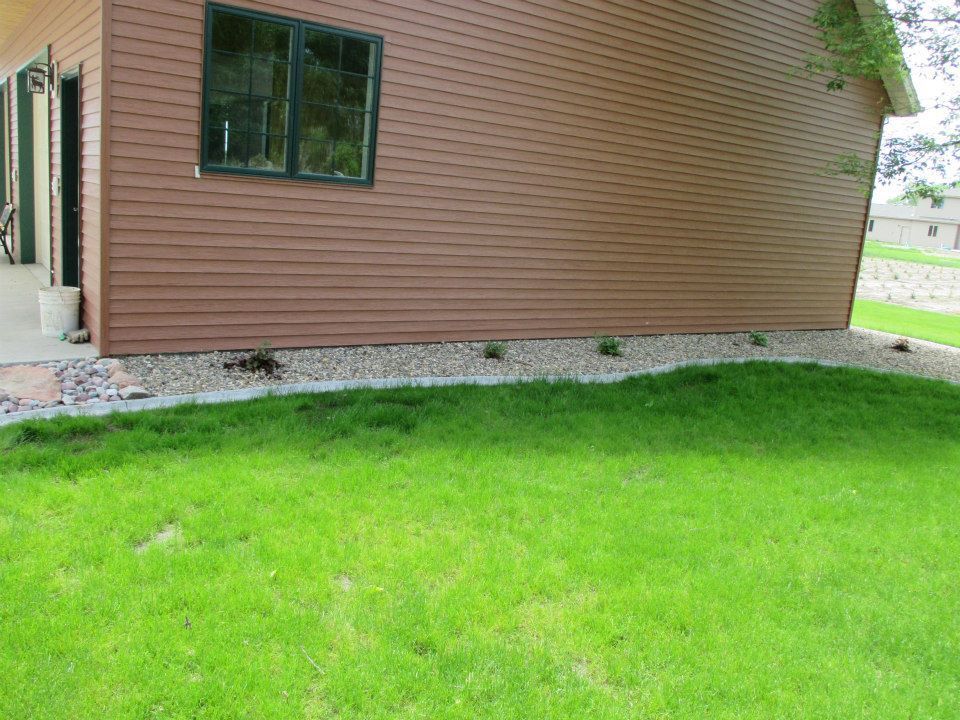 Brown house with green grass, a gravel border, and a single dark green window.