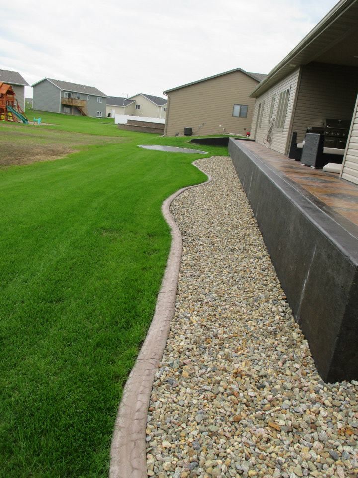 Green lawn with stone border along a house with a gravel bed.