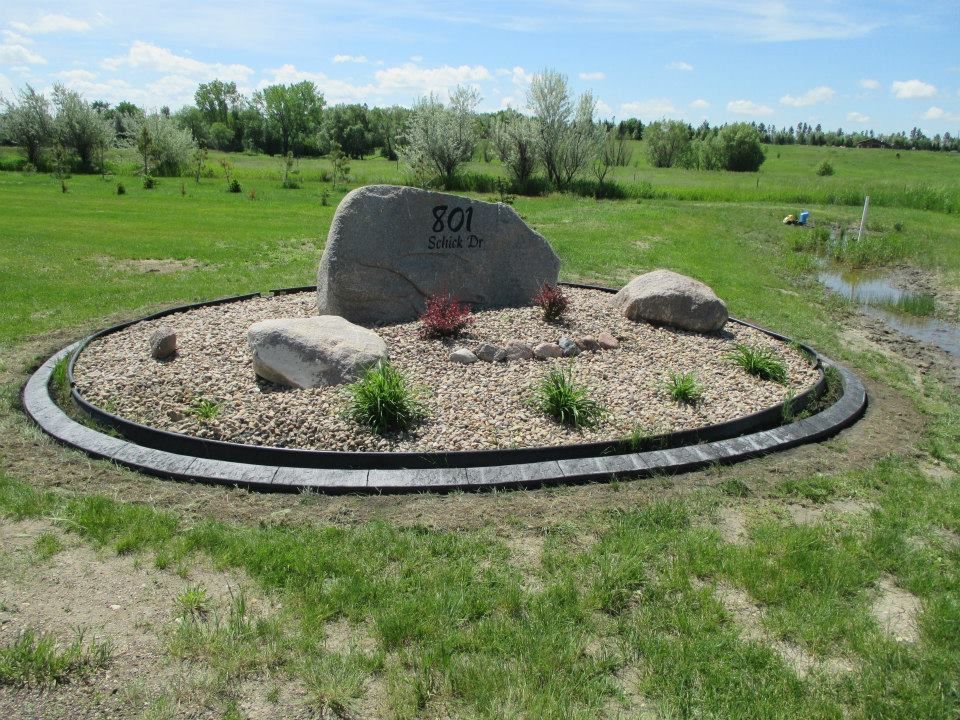 Stone sign in a circular garden bed with address 801, set in a grassy field with trees in the background.