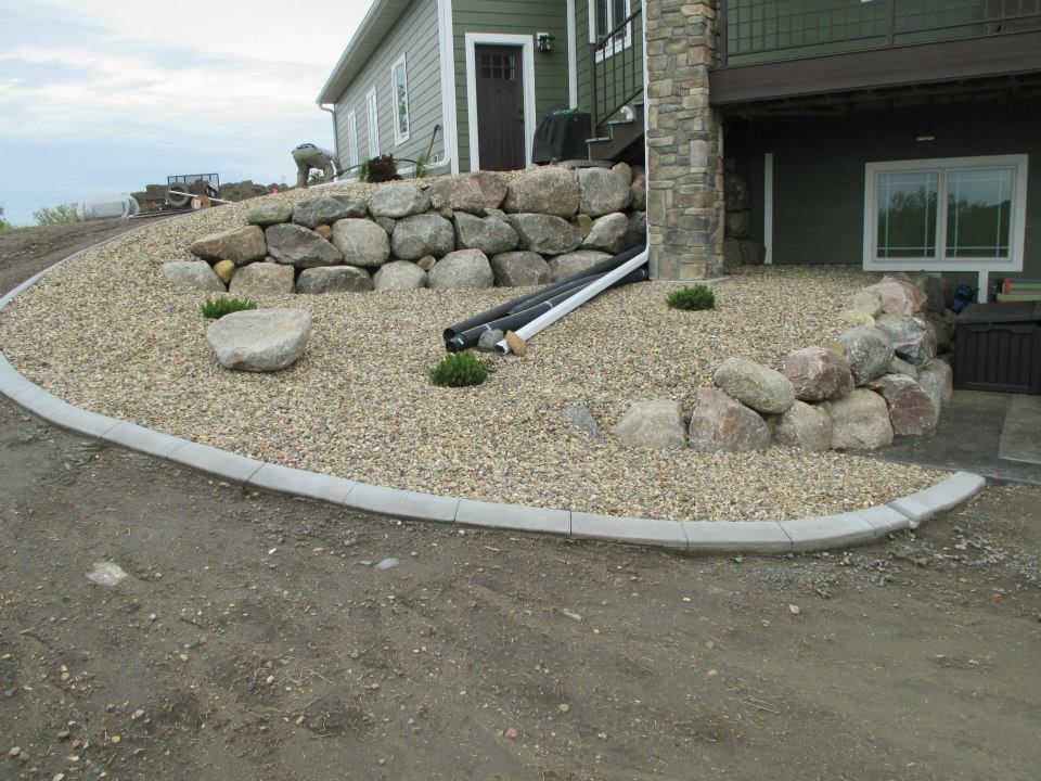 Landscaped yard with rock retaining walls, gravel, and drainage near a house.