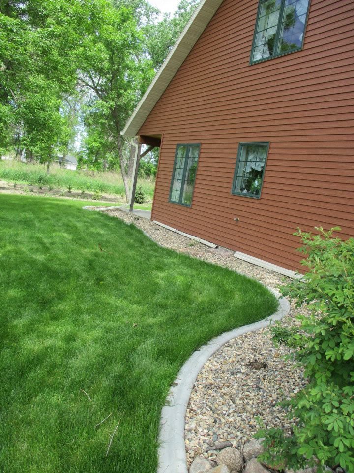 Red-sided house with green-trimmed windows, next to a grassy lawn bordered by stone and a small bush.