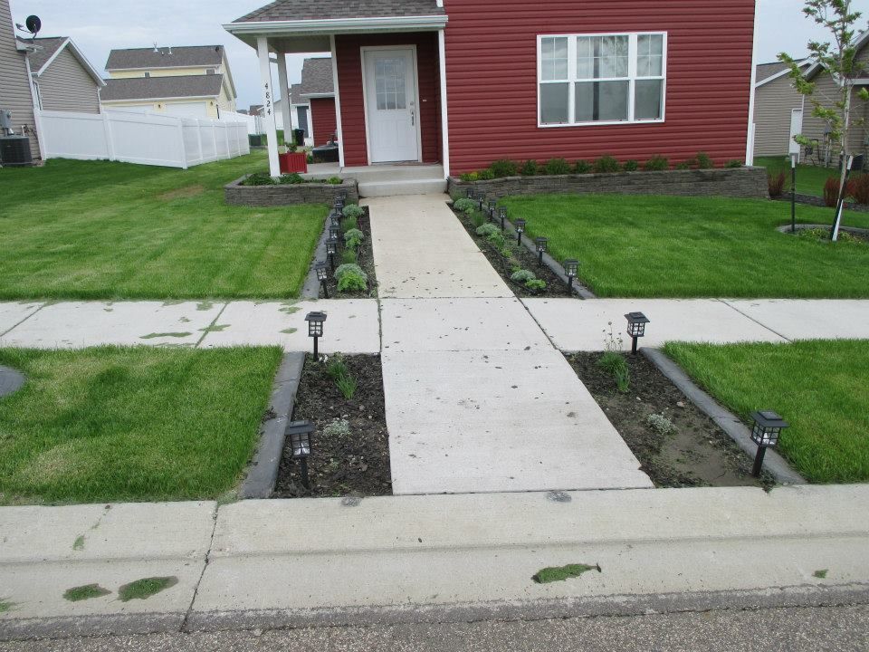 Red house with a concrete path, flanked by small flower beds with solar lights.