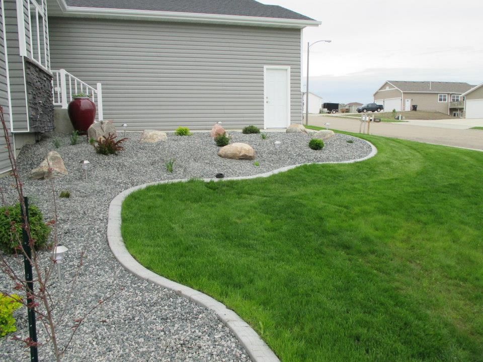 A landscaped yard with gray gravel, rocks, and green grass, curving around the house.