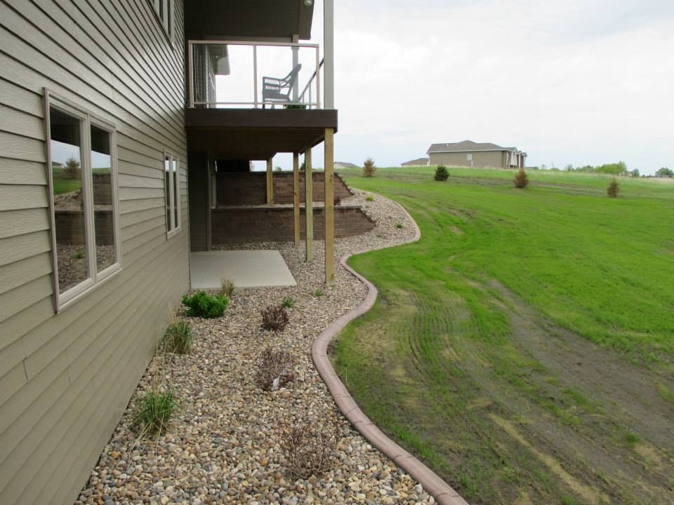 House exterior with a deck, landscaping, and a grassy hill.