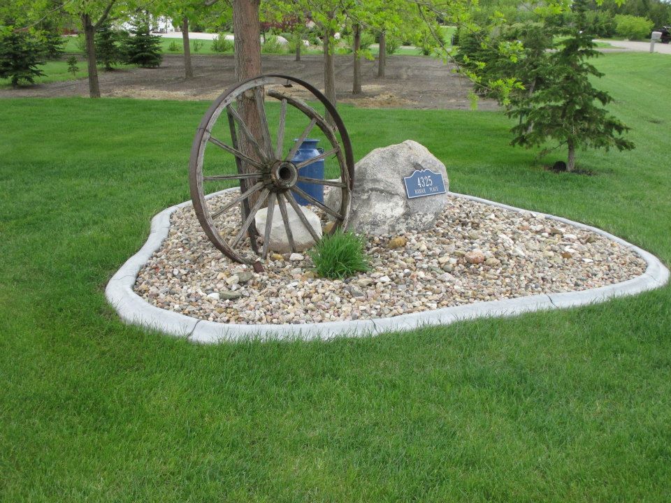 A decorative rock garden with an antique wagon wheel, rock, and small plants on green grass.