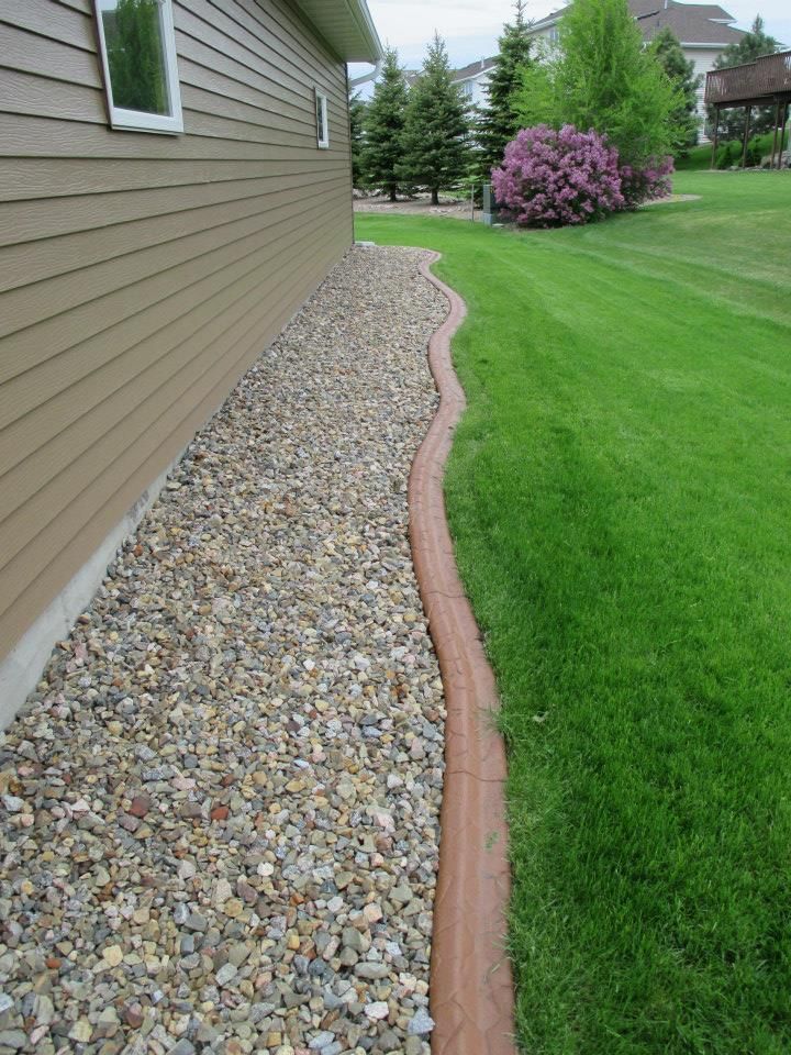 Tan house siding next to a gravel bed bordered by a reddish-brown curb and green lawn.