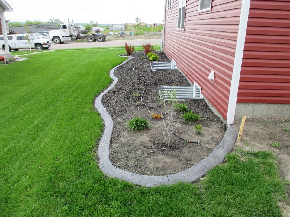 Red house with a landscaped garden bed edged with gray blocks, lush green lawn.
