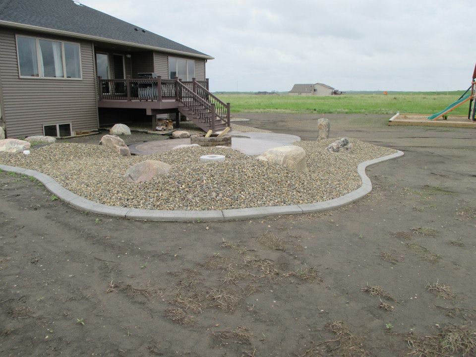 A backyard with a gravel landscaping border around a concrete patio and a house.