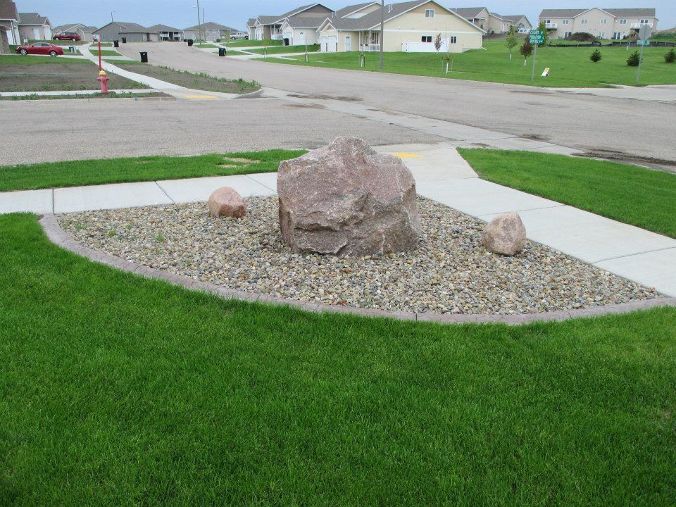 Rock garden in a suburban neighborhood with a large pink rock and two smaller rocks.