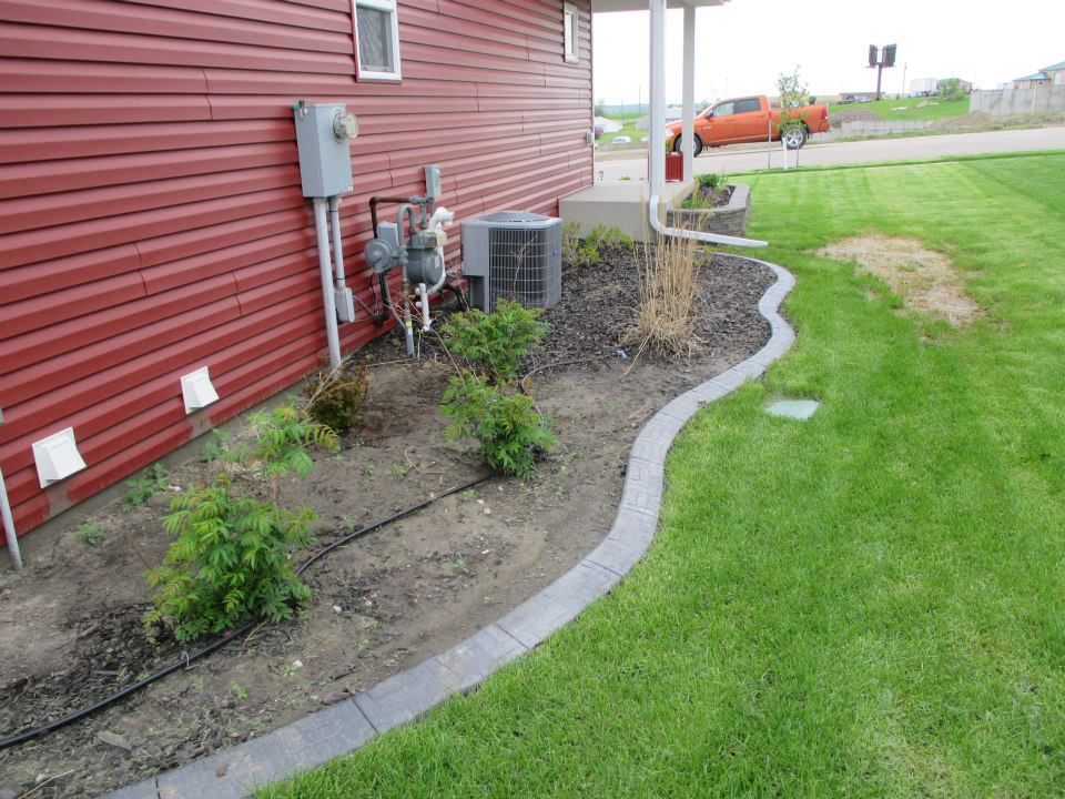 Red house with a landscaped bed, gray edging, and green lawn.