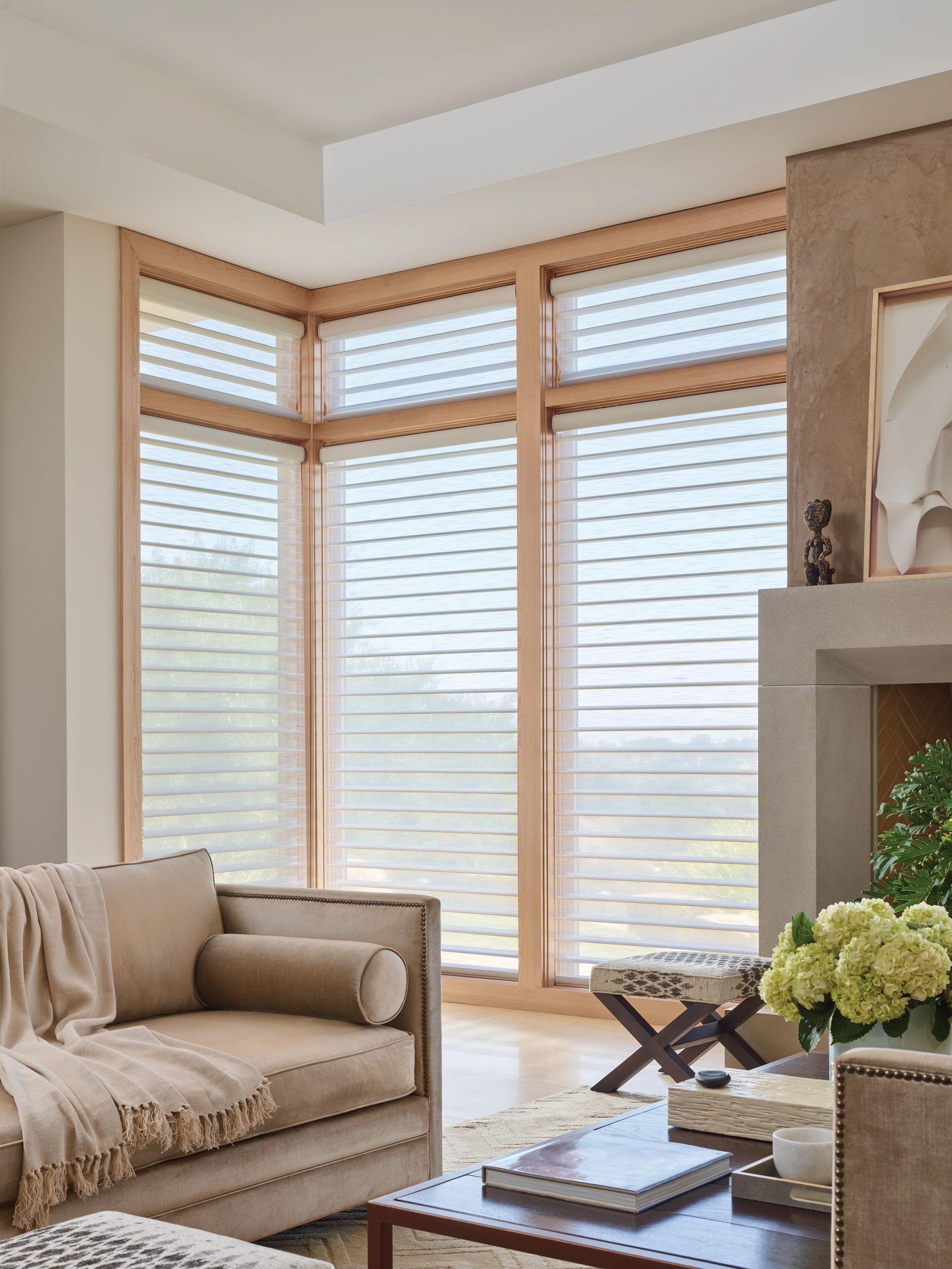 Living room with large windows, light brown sofa, neutral tones, sheer window coverings, and fireplace.