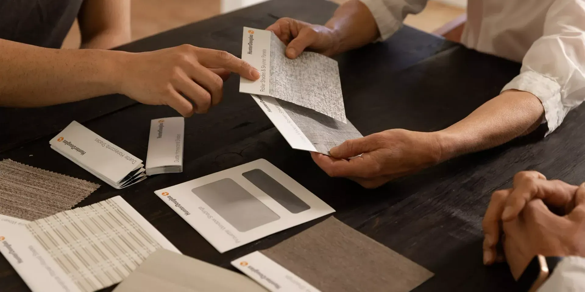 Hands examining material samples on a dark table, likely for interior design choices.