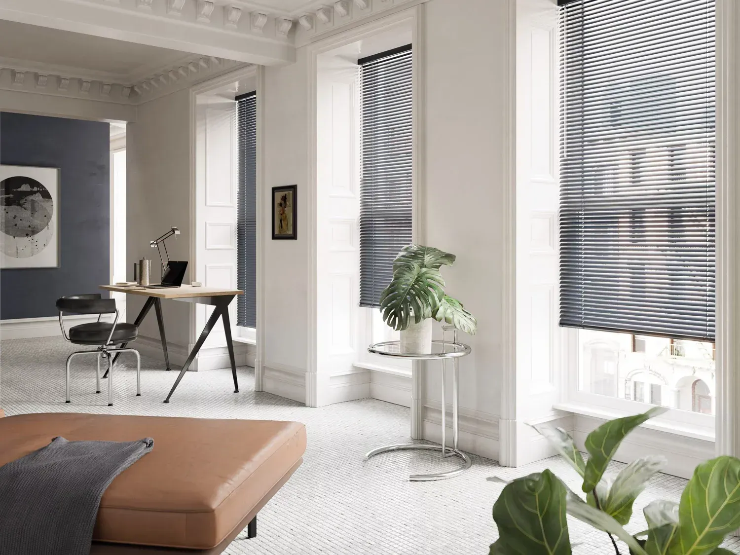 A bright room with large windows, blinds, and plants. A desk and a leather couch complete the scene.