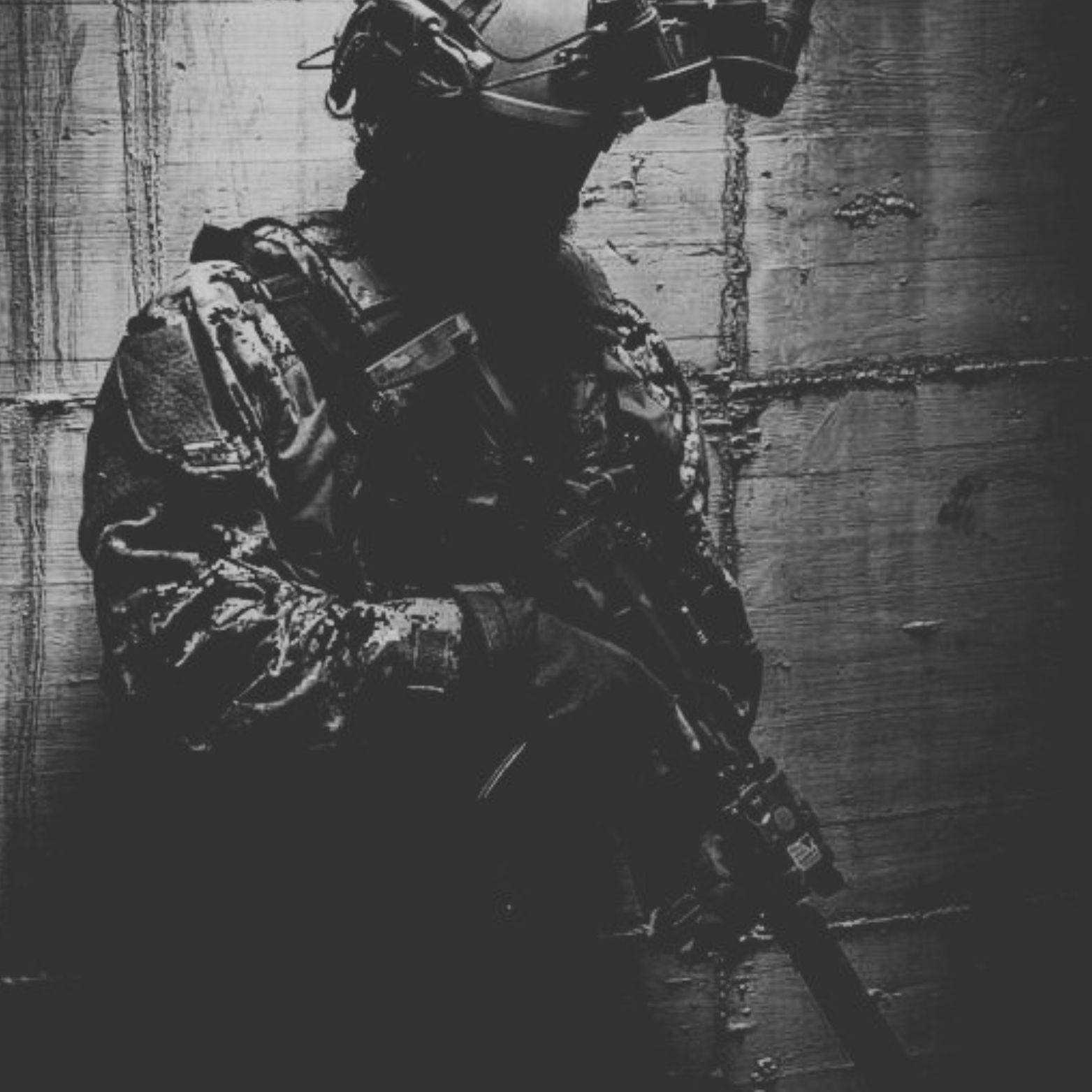 Soldaat in tactische uitrusting met een geweer, leunend tegen een muur. Zwart-wit.