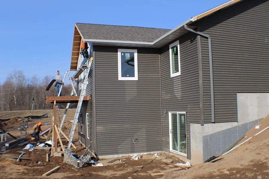 Workers construct a balcony on a dark-sided two-story house under construction in a rural area.