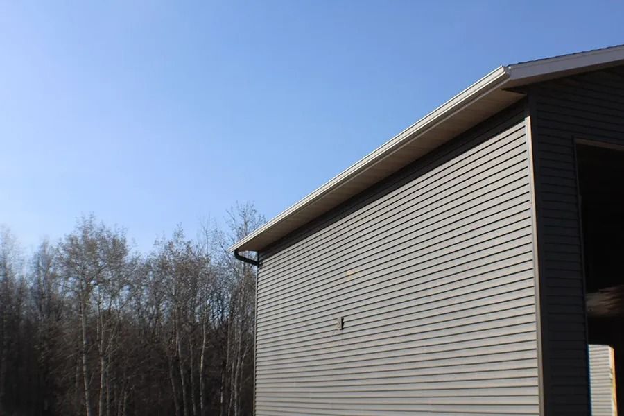 A grey, vinyl-sided building exterior sits against a clear blue sky, next to a line of bare trees.