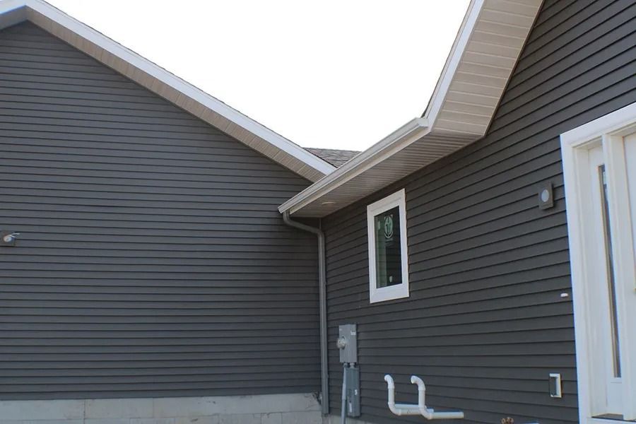 A corner of a modern house exterior with dark horizontal siding, a white-framed window, and a white doorway.