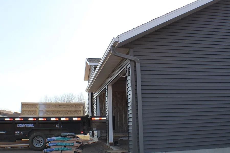 A trailer loaded with construction materials parked next to a house with dark gray siding.
