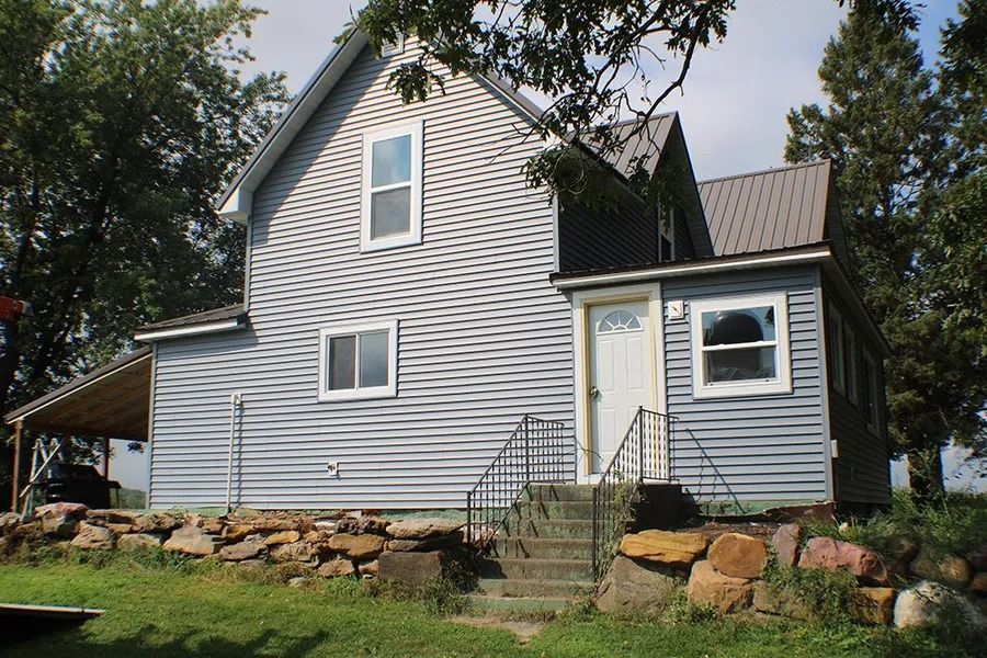 A two-story blue house with light siding and a metal roof, featuring stone landscaping and a small set of concrete steps.