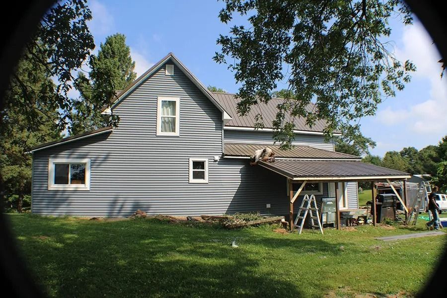 A grey two-story house with a metal-roofed porch, seen through a circular lens vignette on a sunny day.