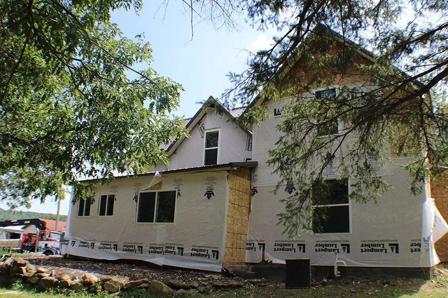 A house under construction with white protective wrap on its exterior walls and newly installed windows.