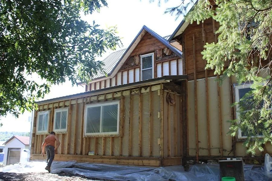 A person walks past a house under construction, featuring exposed wooden wall studs and newly installed windows.