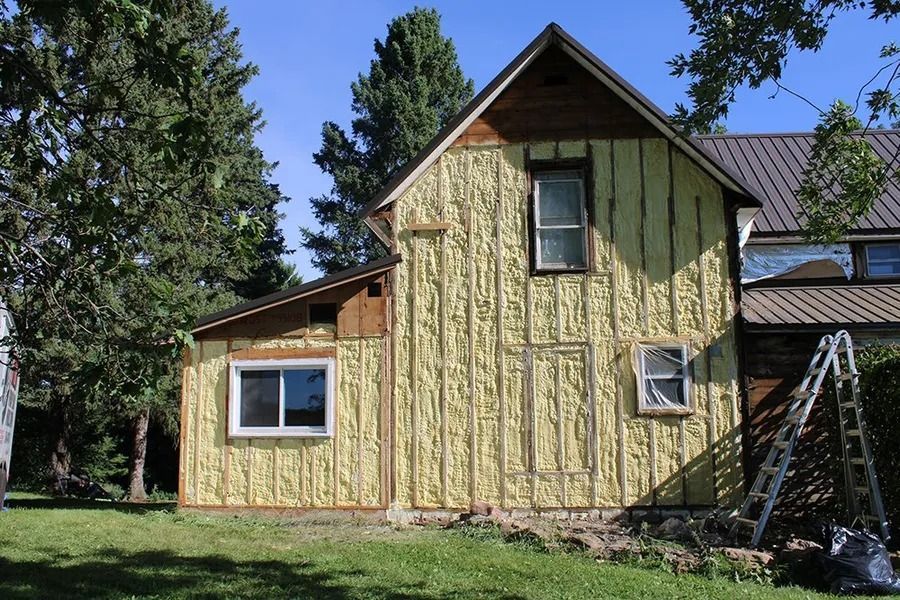 The exterior wall of a house undergoing renovations, covered with yellow spray foam insulation and vertical wooden slats.