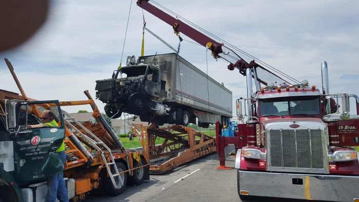 A truck is being towed by a crane on the side of the road.