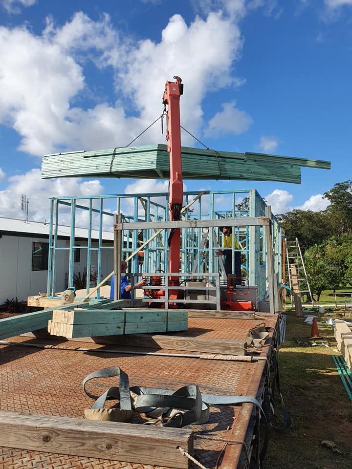 Crane Lifting Wooden Beams To Frame A New House On A Flatbed Truck. Sunny Day With Blue Sky