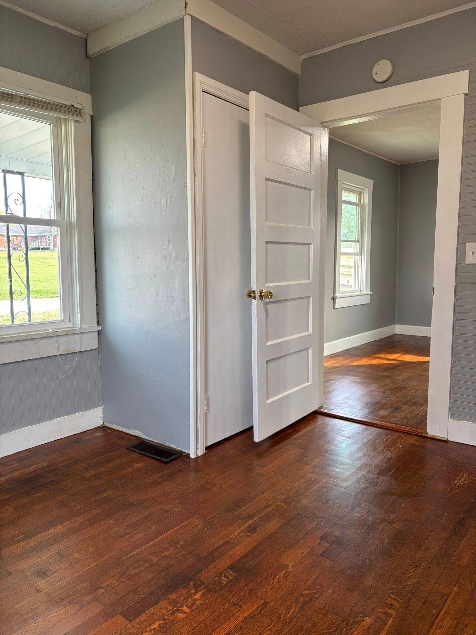 Room interior with wood floors, closet, open doorway to another room, and windows.