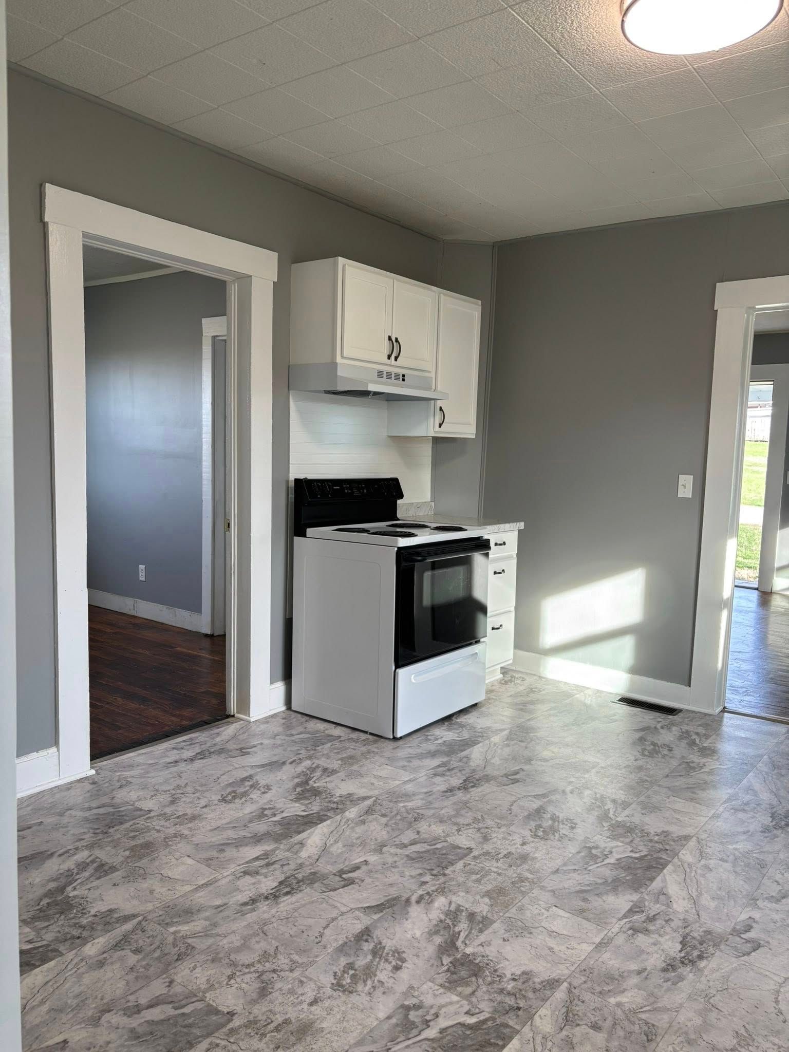 Small kitchen with gray walls, white cabinets, and a white stove. Two doorways visible.