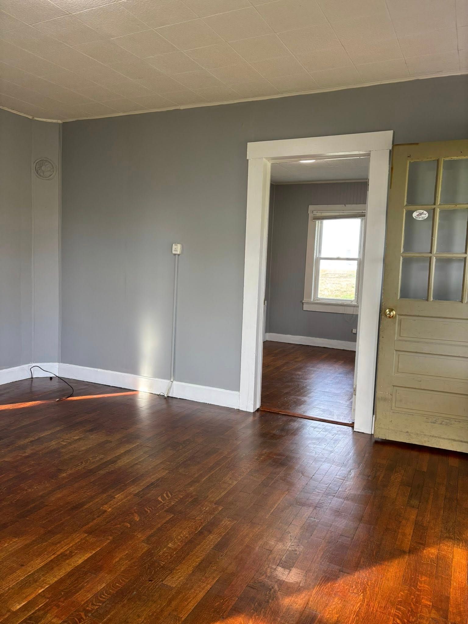 Empty room with gray walls, hardwood floor, open doorway to another room, and a door on the right.