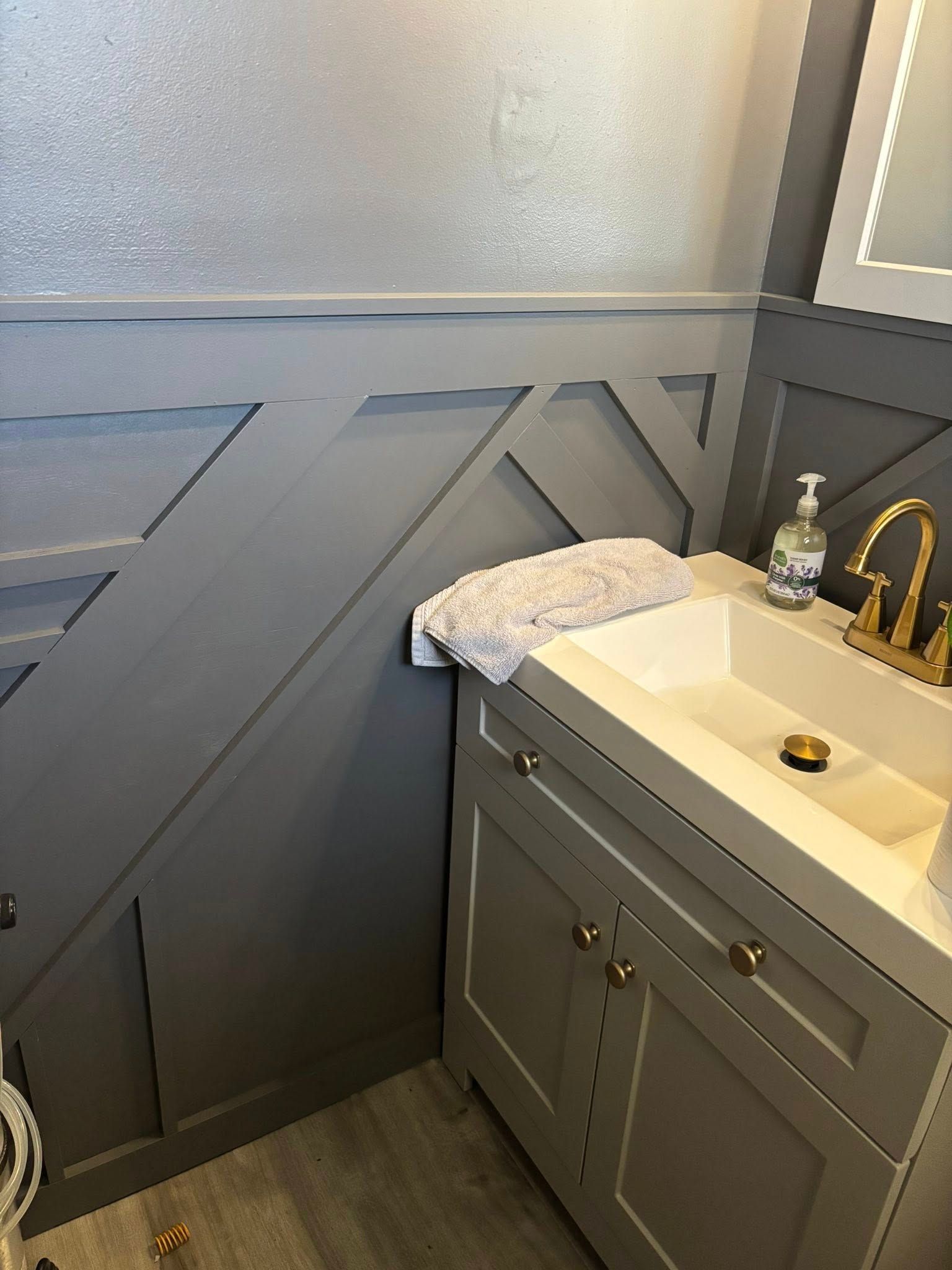 Gray bathroom with a sink, cabinet, and geometric wall paneling. A towel rests on the counter.