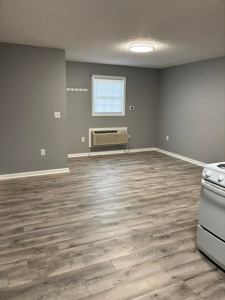 Empty room with gray walls, wood-look flooring, window, and wall-mounted air conditioner.