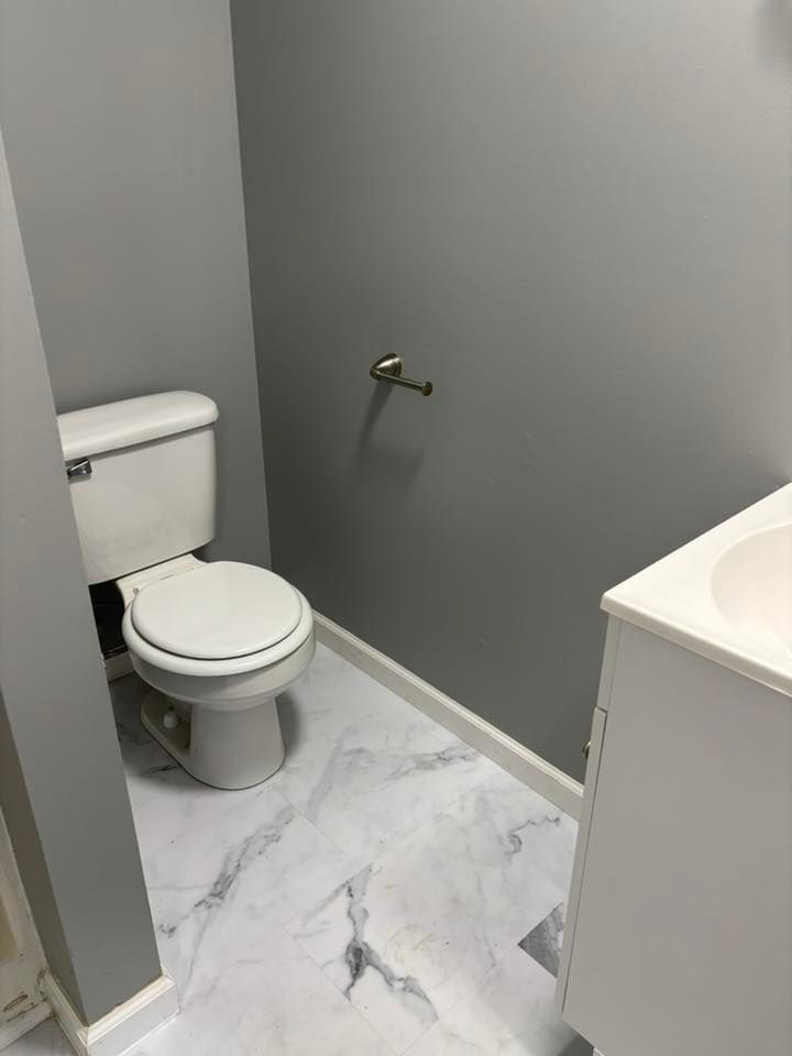 Bathroom with white toilet, marble-patterned floor, gray walls, and white sink cabinet.