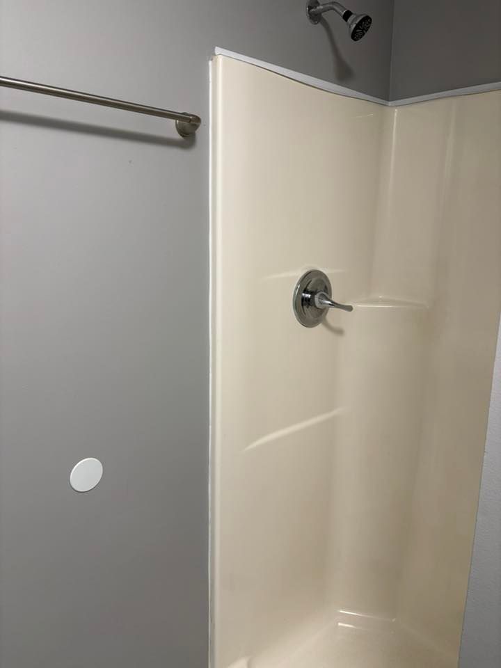 Shower stall with tan walls, chrome fixtures, and a gray wall with a towel rack.