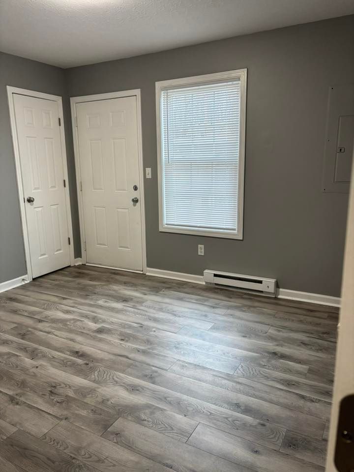 Empty room with gray walls, light wood-look flooring, white doors, and a window with blinds.
