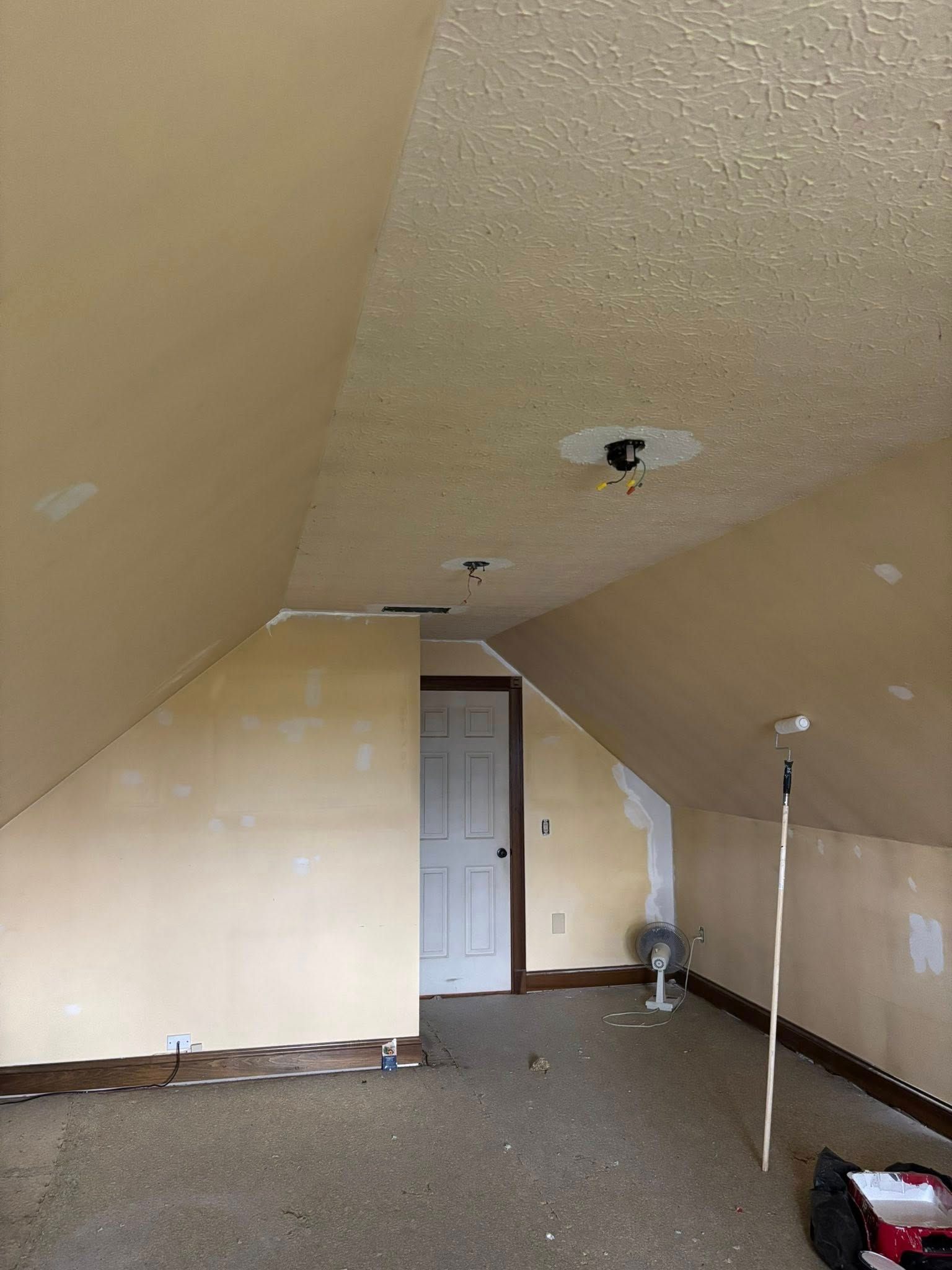 Beige attic room with sloped walls, a door, and a textured ceiling.