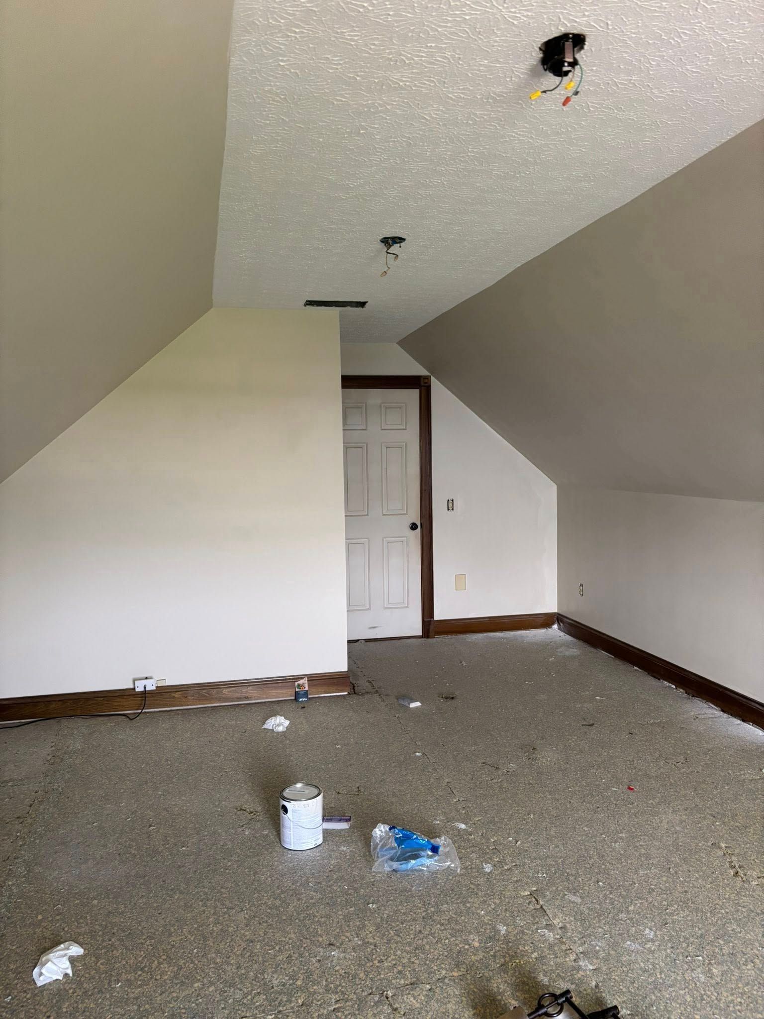 Attic room with sloped walls, a door, and textured ceiling. Paint and debris on the speckled floor.
