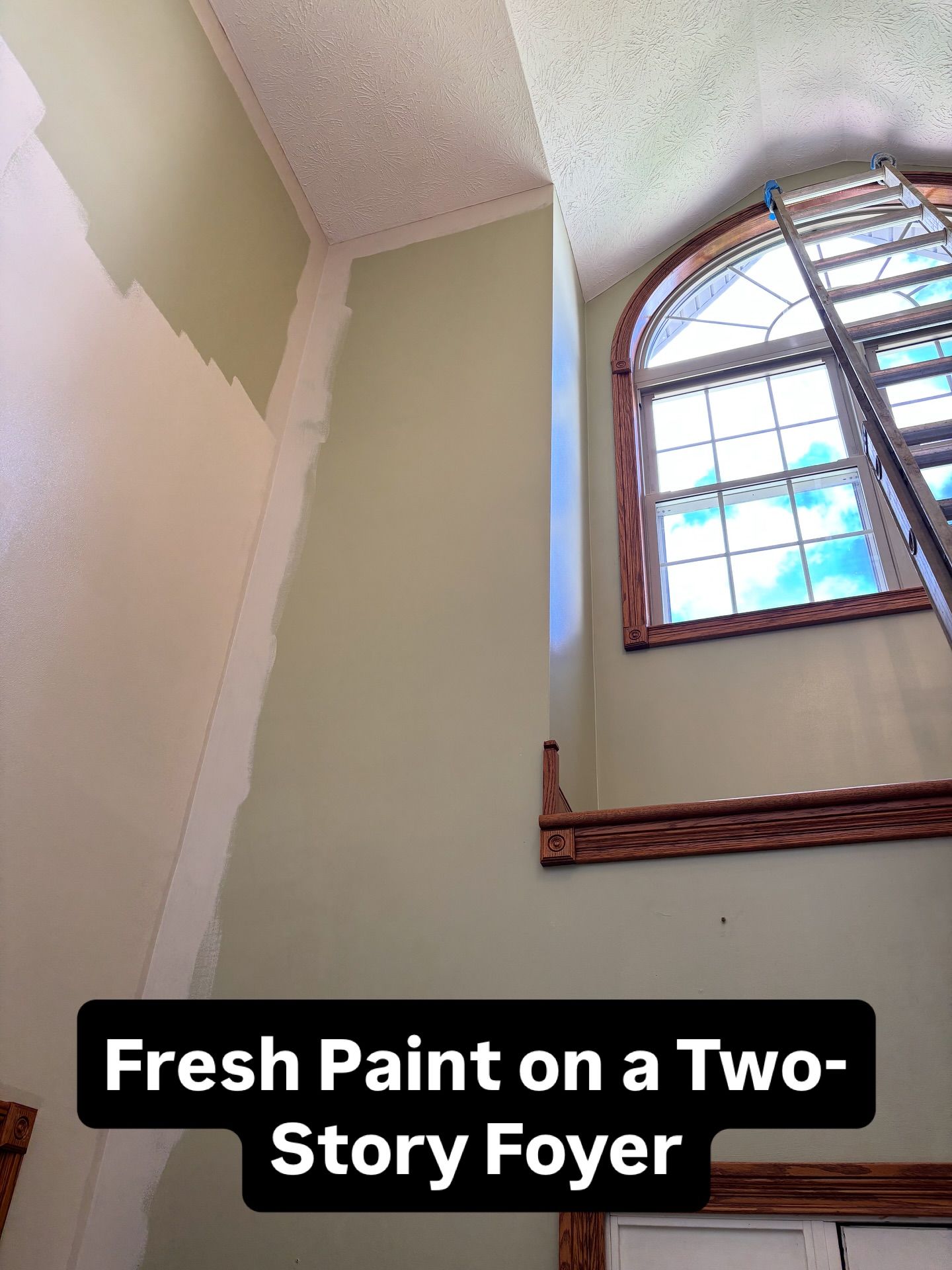 Two-story foyer with fresh green paint and a ladder by an arched window.