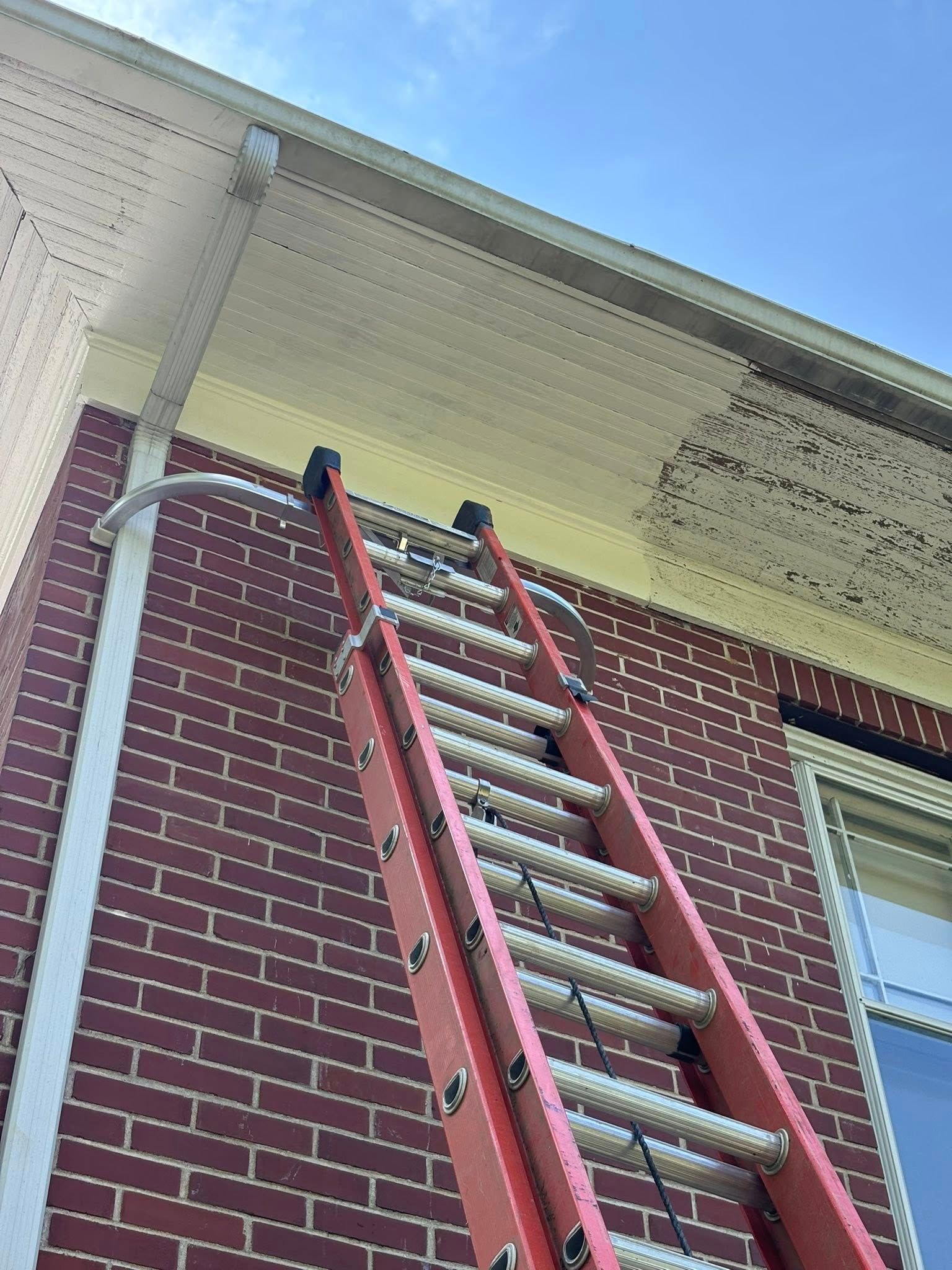 Red ladder leaning against a brick building, reaching toward the white eaves.