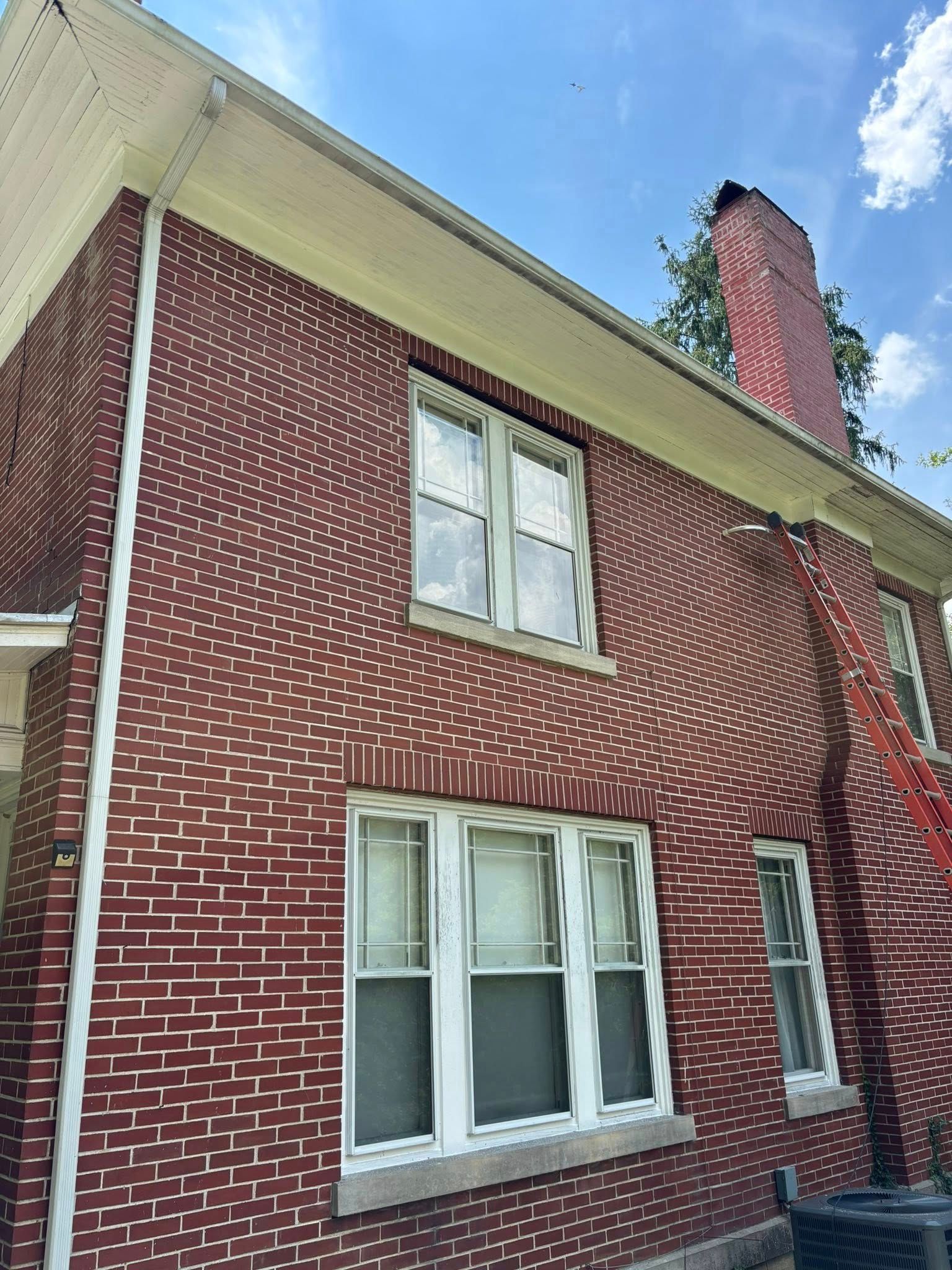 Red brick house with white trim and chimney against a blue sky.